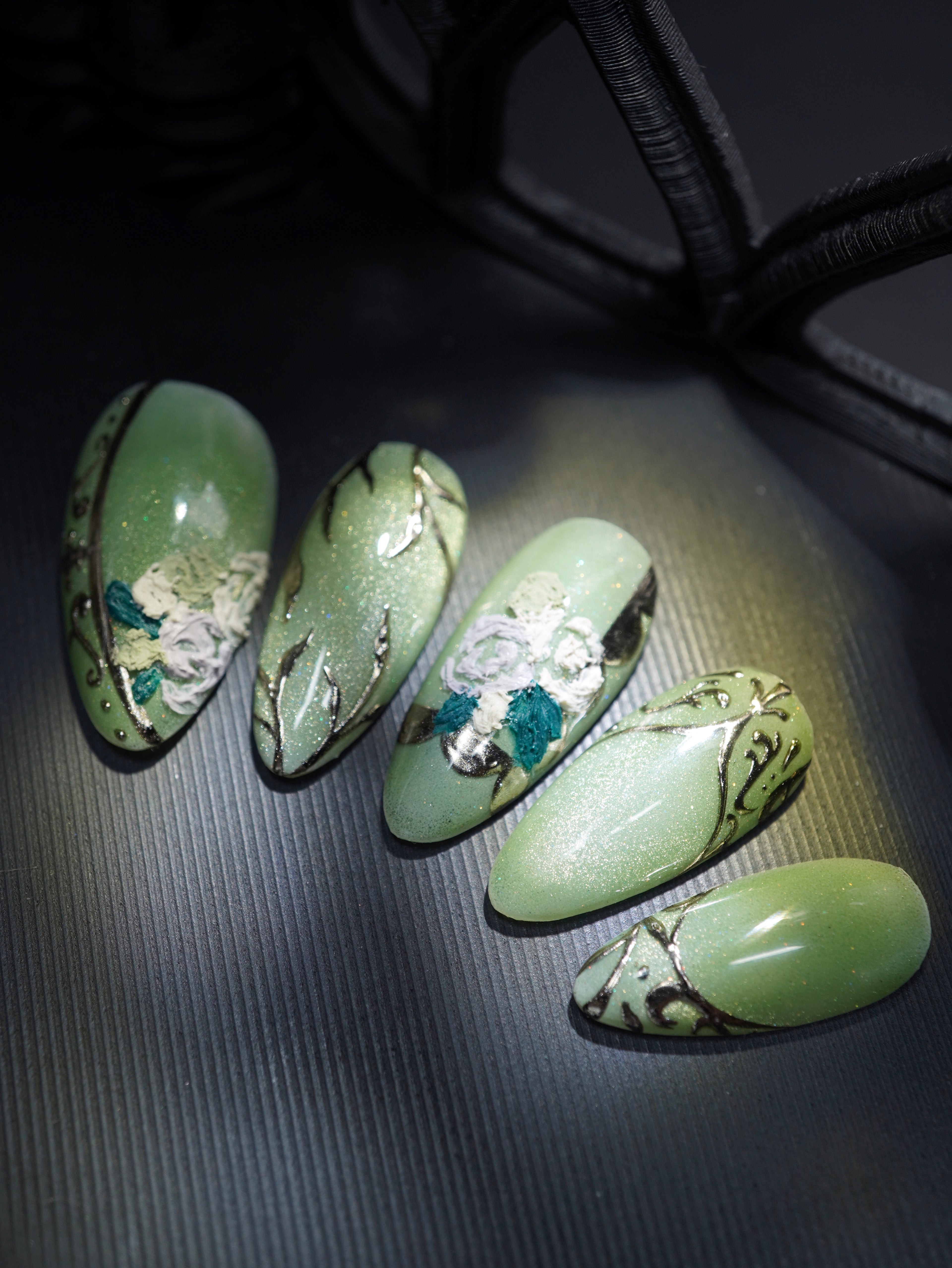 april's monthly subscription design, featuring a holographic green base and champagne gold ornate accents. topped with textured roses in green, lavender, and cream.